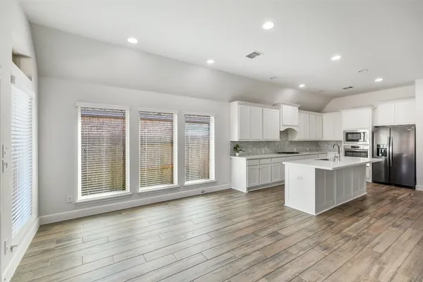 a large kitchen with kitchen island wooden floors white cabinets and stainless steel appliances