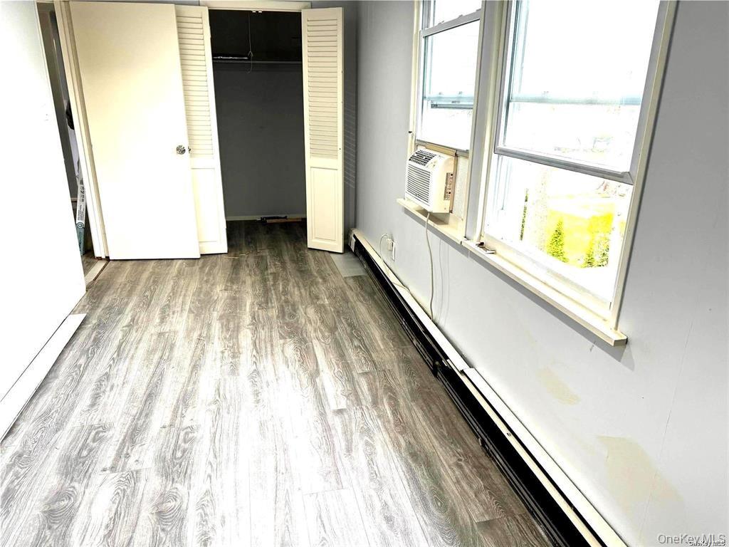107 Baker Hill Road Great Neck, NY 11023 - Photo 20 of 33 Unfurnished bedroom featuring a baseboard radiator, dark wood-style flooring, cooling unit, and a closet