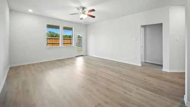 an empty room with wooden floor chandelier fan and windows