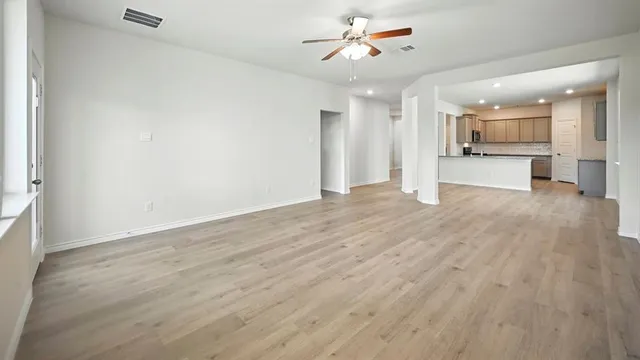 an empty room with wooden floor chandelier fan and windows