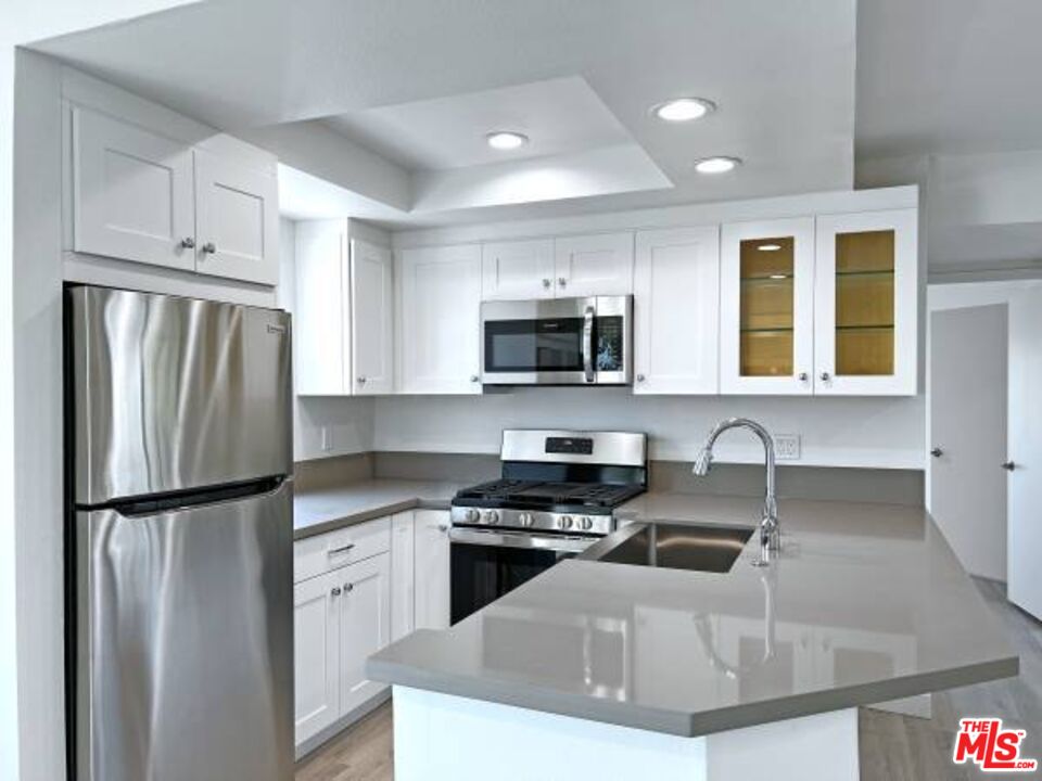 a kitchen with granite countertop a refrigerator a sink a stove a microwave and cabinets