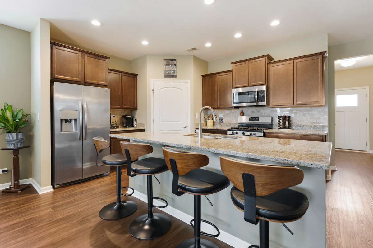 1150 Americana Avenue Pingree Grove, IL 60140 - Photo 6 of 30 a kitchen with stainless steel appliances granite countertop a refrigerator a stove a sink and a dining table with wooden floor
