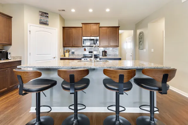 a kitchen with stainless steel appliances granite countertop a sink a stove a kitchen island with chairs and wooden floor