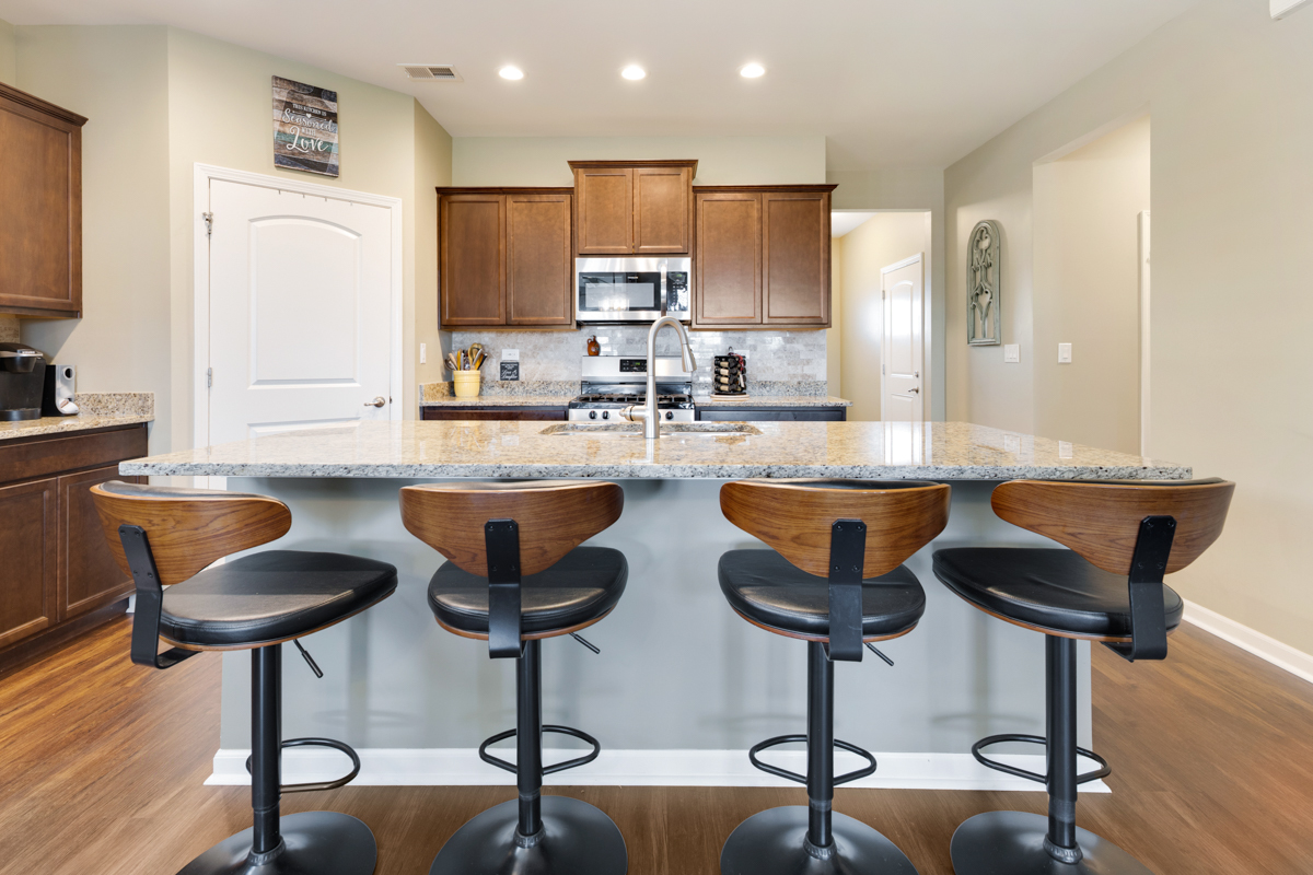 1150 Americana Avenue Pingree Grove, IL 60140 - Photo 7 of 30 a kitchen with stainless steel appliances granite countertop a sink a stove a kitchen island with chairs and wooden floor