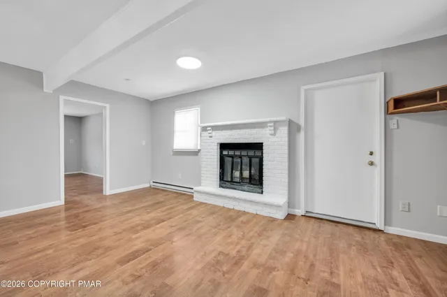 a view of an empty room with wooden floor fireplace and a window