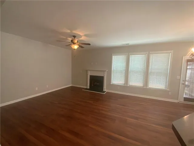 an empty room with wooden floor fan and windows