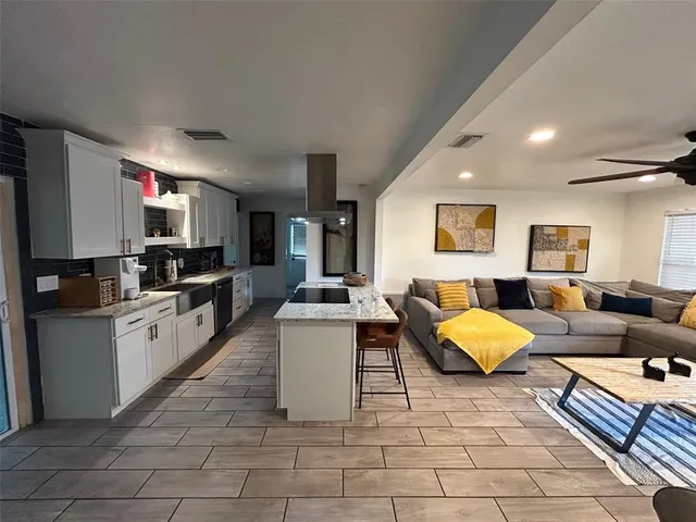 a large white kitchen with kitchen island granite countertop a living room filled with furniture and a couch