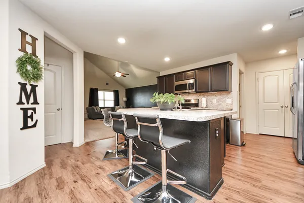 a kitchen with stainless steel appliances granite countertop a refrigerator a stove top oven a sink dishwasher and white cabinets with wooden floor