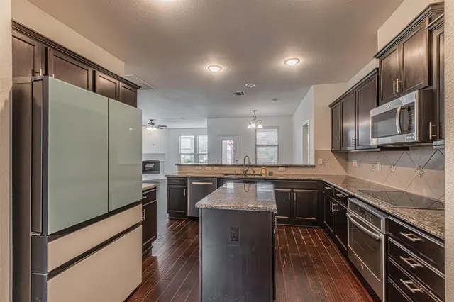 a kitchen with stainless steel appliances granite countertop a refrigerator a stove and a sink with wooden floor