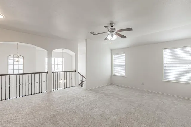 an empty room with chandelier fan and windows