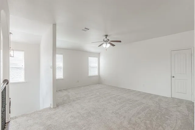 an empty room with chandelier fan and windows