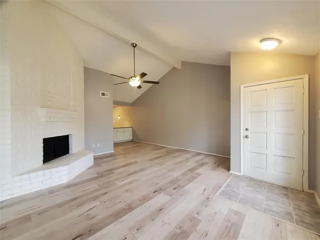an empty room with wooden floor fireplace and windows