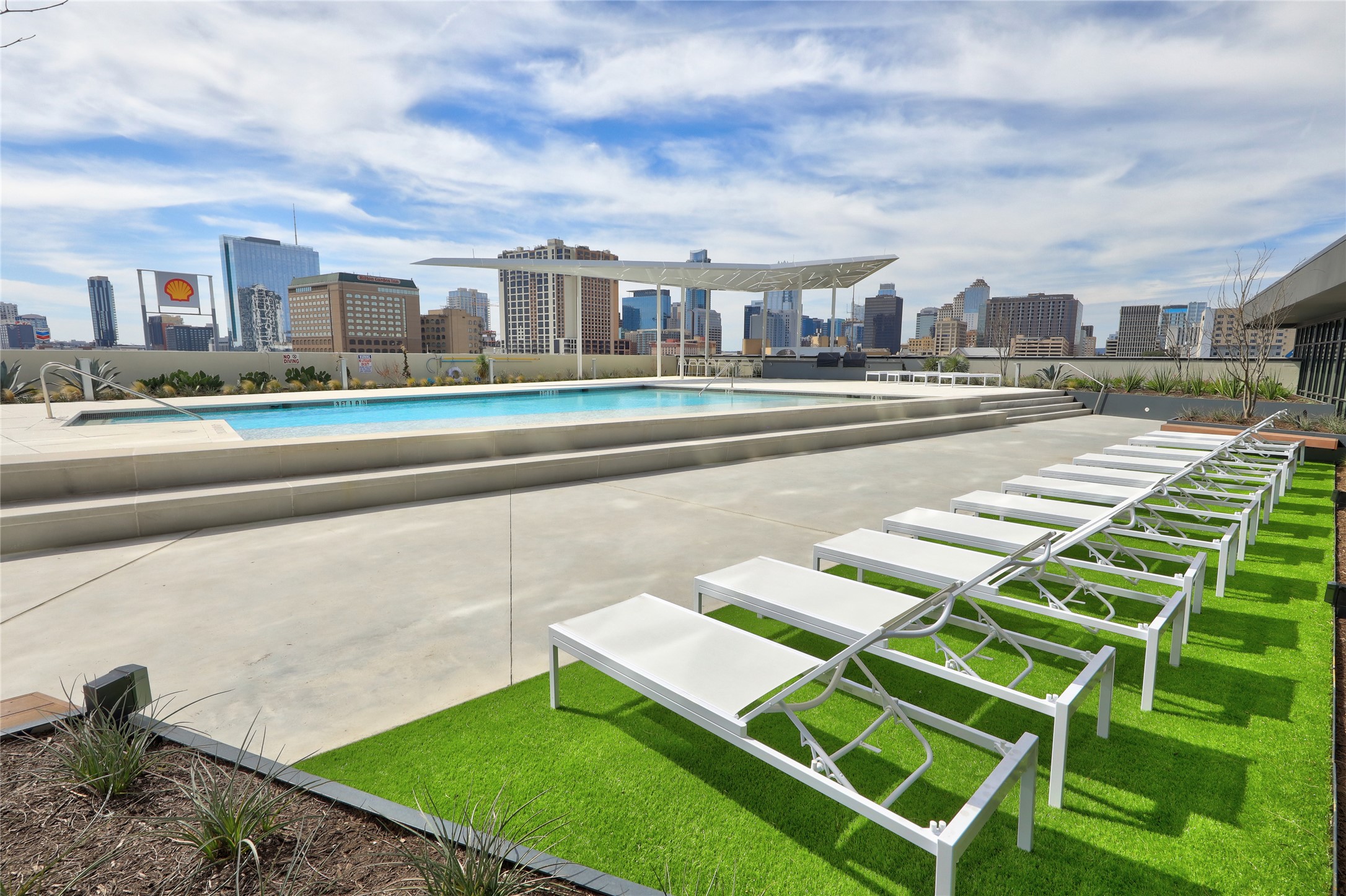 800 Embassy Drive, Unit 602 Austin, TX 78702 - Photo 25 of 37 Rooftop amenity space featuring a rectangular swimming pool, concrete decking, and a row of lounge seating on artificial turf