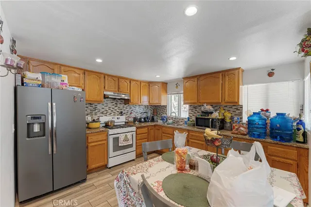 a kitchen with stainless steel appliances granite countertop a refrigerator a sink a stove a dining table and chairs
