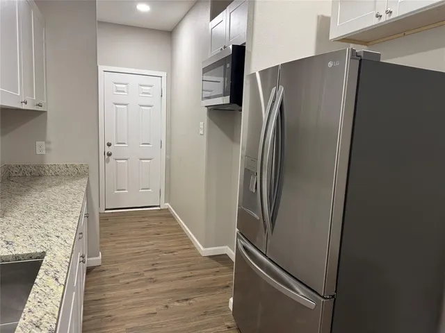 a view of a refrigerator in kitchen and an empty room with wooden floor