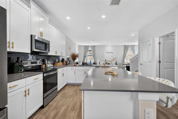 a kitchen with stainless steel appliances granite countertop a refrigerator a sink dishwasher a stove and white cabinets with wooden floor