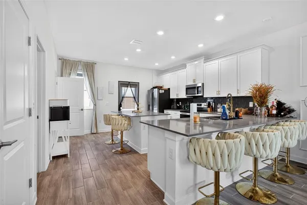 a kitchen with stainless steel appliances kitchen island granite countertop a refrigerator a stove a sink and white cabinets with wooden floor