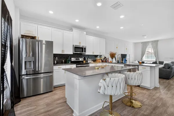 a kitchen with stainless steel appliances granite countertop a refrigerator a stove a sink a dining table and chairs