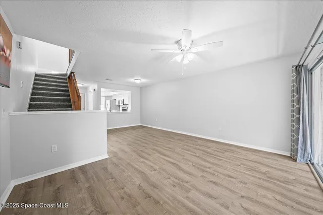 an empty room with wooden floor fan and windows