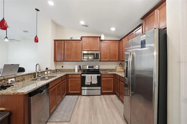 a kitchen with stainless steel appliances granite countertop a refrigerator a sink dishwasher a stove and white cabinets with wooden floor