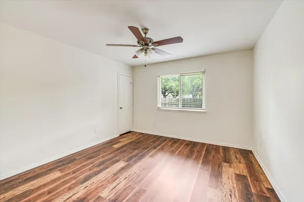 an empty room with wooden floor ceiling fan and windows