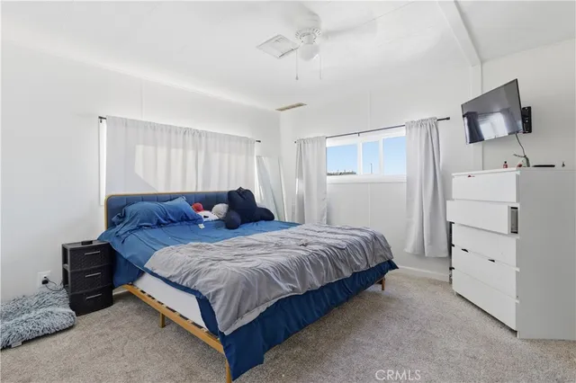 a spacious bedroom with a bed and a flat tv screen on dresser