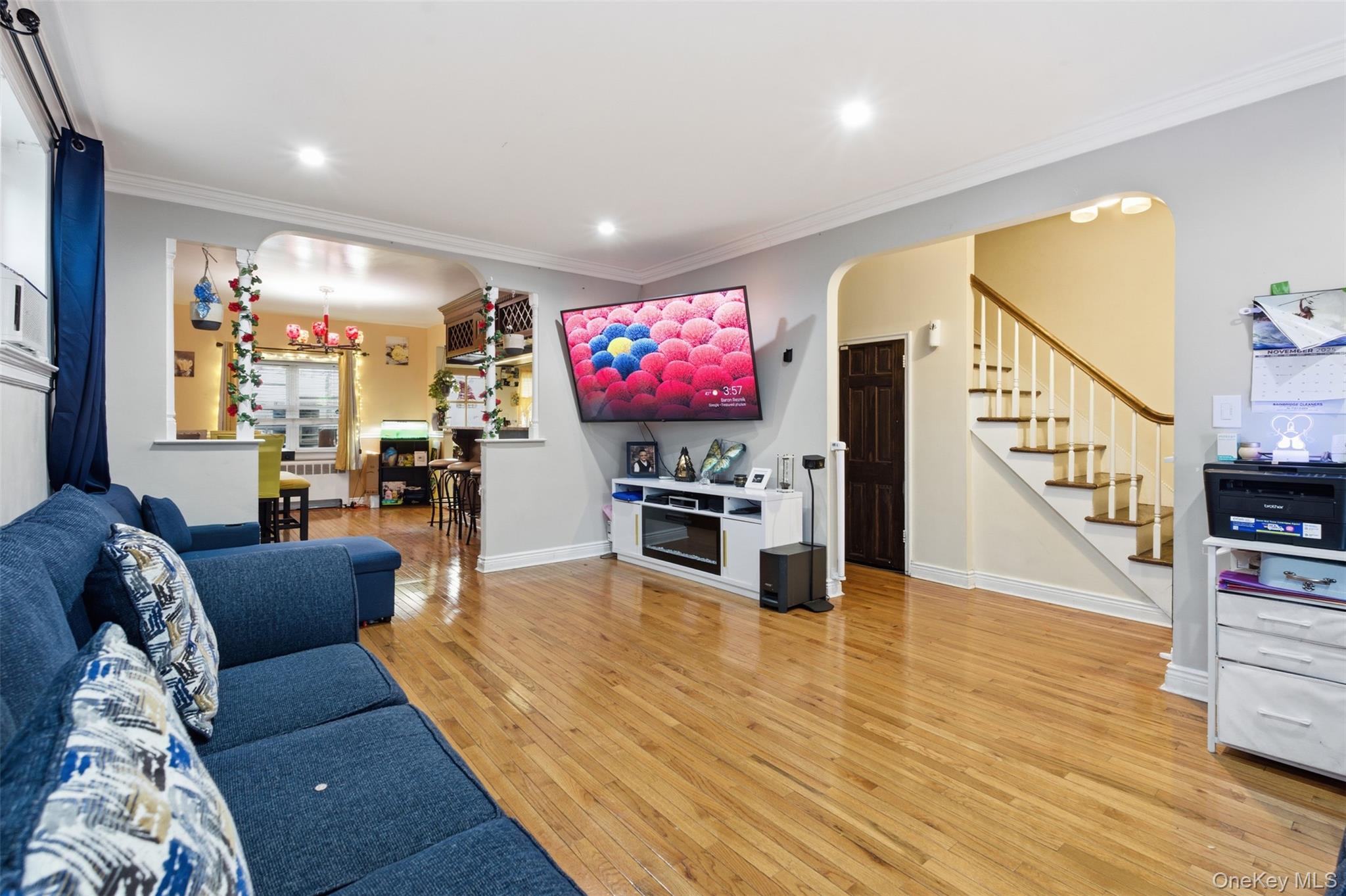 1408 Astor Avenue Bronx, NY 10469 - Photo 5 of 21 Living room with arched walkways, light wood-style floors, stairs, radiator, and crown molding