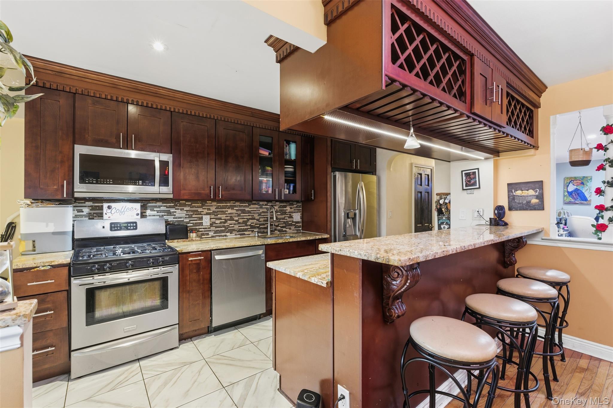1408 Astor Avenue Bronx, NY 10469 - Photo 7 of 21 Kitchen featuring a breakfast bar, light stone counters, stainless steel appliances, glass insert cabinets, and a peninsula