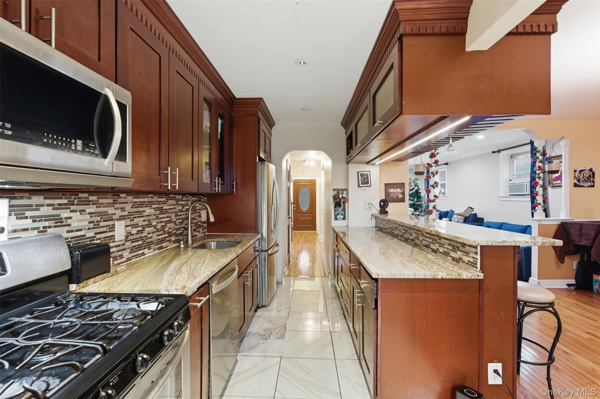 1408 Astor Avenue Bronx, NY 10469 - Photo 8 of 21 Kitchen featuring appliances with stainless steel finishes, arched walkways, light stone countertops, a kitchen breakfast bar, and glass insert cabinets