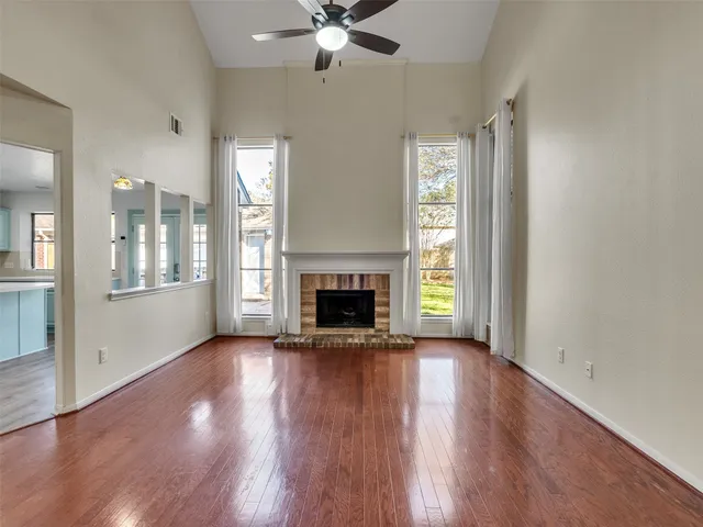 an empty room with wooden floor fireplace and windows