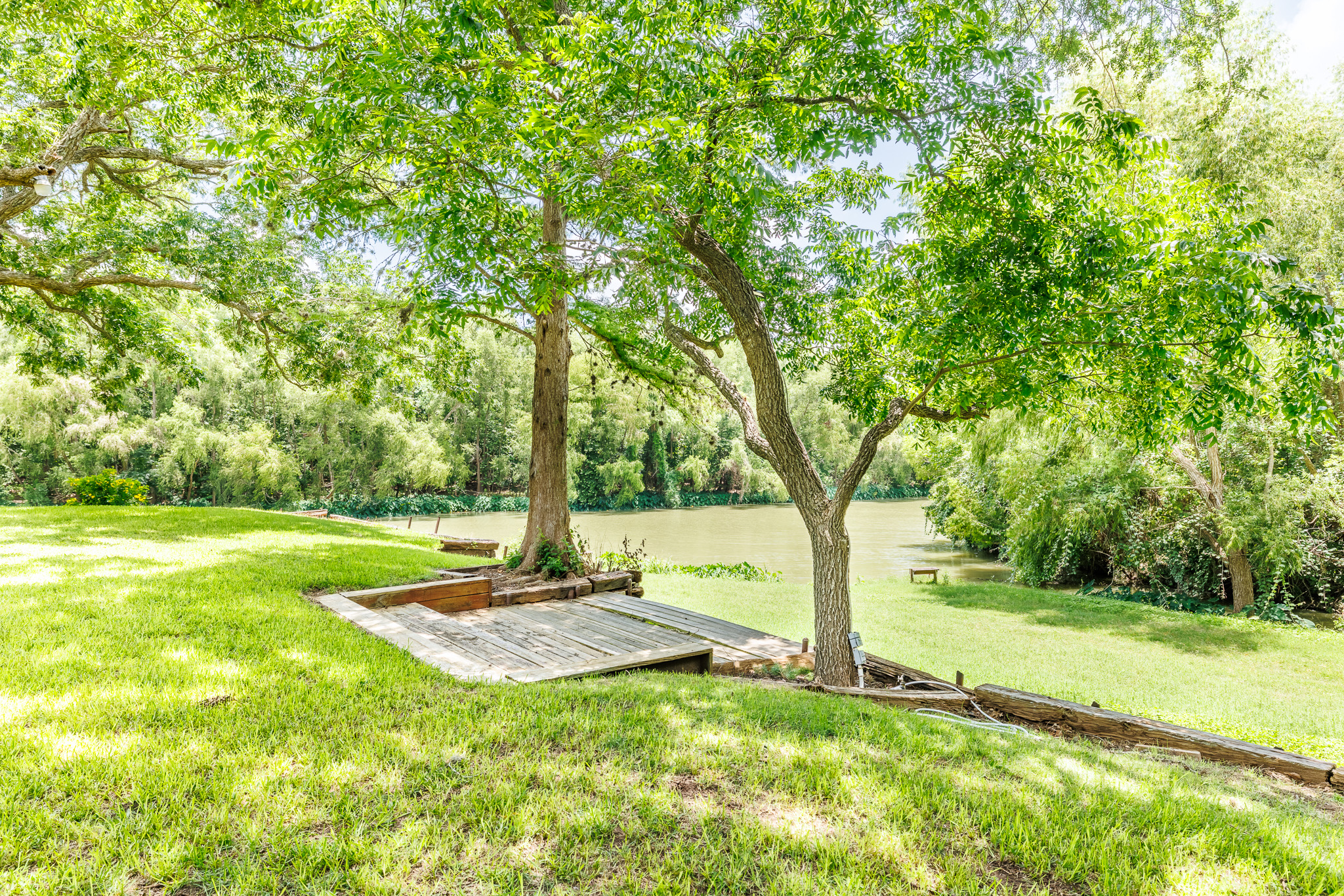 Tbd Goodwin Road Gonzales, TX 78629 - Photo 8 of 33 A tranquil outdoor haven unfolds with verdant lawn and mature trees beside a peaceful waterfront.