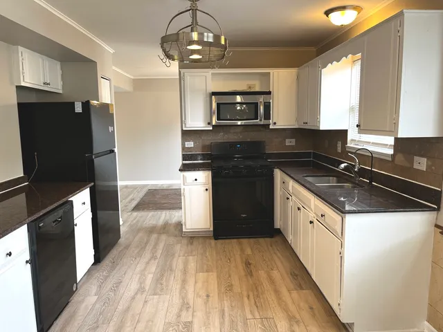 a kitchen with stainless steel appliances a sink dishwasher a refrigerator a stove top oven a wooden floor and cabinets