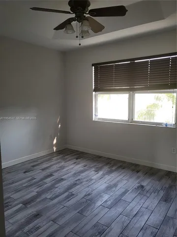 an empty room with wooden floor fan and windows