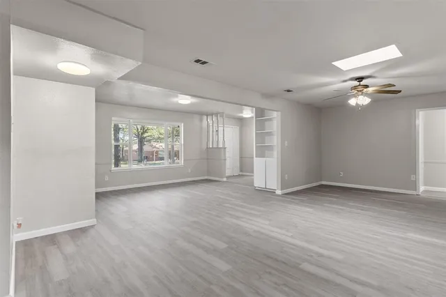 an empty room with wooden floor chandelier fan and windows