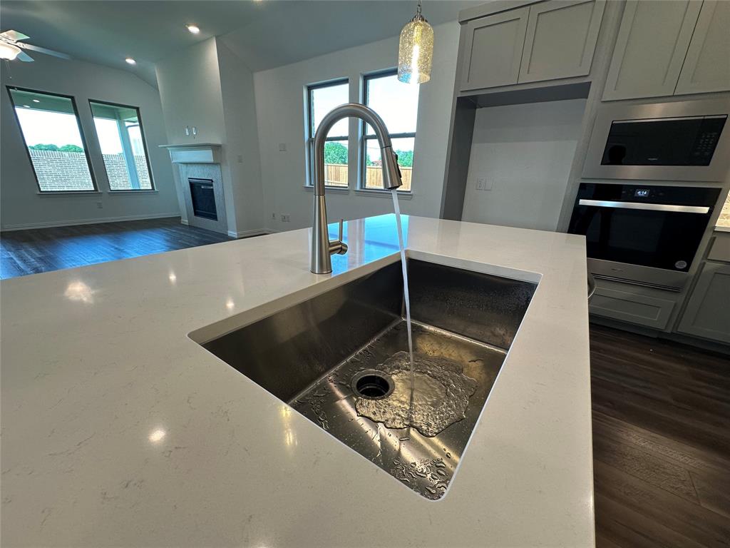 3401 Paintbrush Path Melissa, TX 75454 - Photo 18 of 39 Kitchen featuring dark wood finished floors, stainless steel appliances, light stone countertops, a glass covered fireplace, and decorative light fixtures