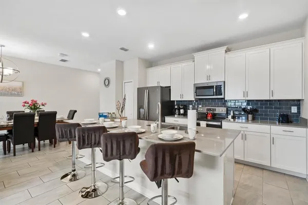 a kitchen with stainless steel appliances kitchen island granite countertop a dining table chairs and a refrigerator