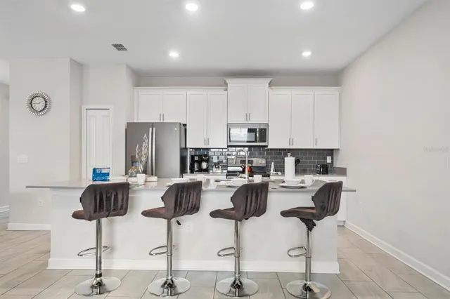 a kitchen with stainless steel appliances kitchen island granite countertop a refrigerator a stove a dining table and chairs with wooden floor