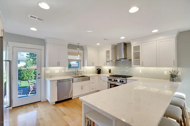 a large kitchen with kitchen island a stove a sink a refrigerator and white cabinets with wooden floor