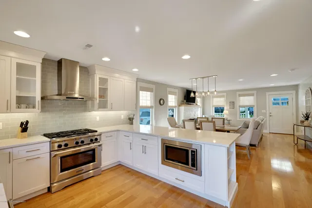 a kitchen with stainless steel appliances granite countertop a stove top oven a sink dishwasher and white cabinets with wooden floor