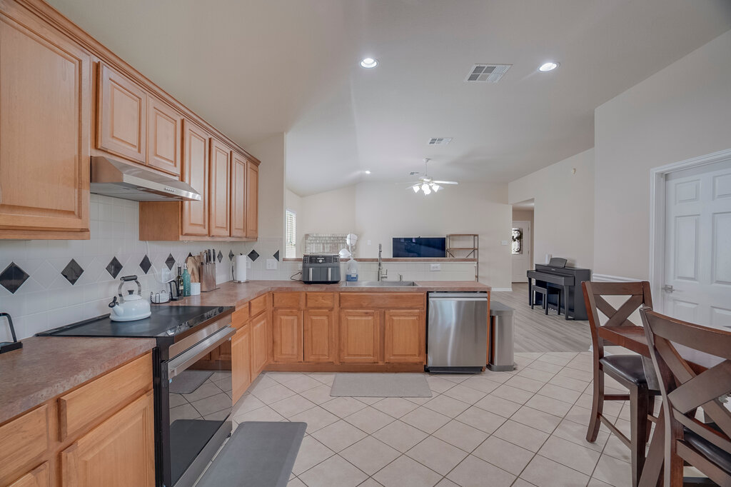 2724 Kickapoo Cavern Drive Pflugerville, TX 78660 - Photo 11 of 24 A well-appointed kitchen features warm wooden cabinetry, a range hood, and a stainless steel dishwasher, opening into a spacious living area.
