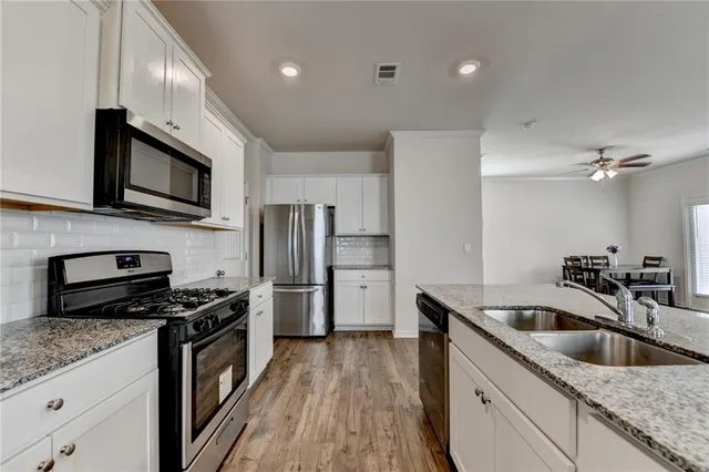 a kitchen with stainless steel appliances granite countertop a sink a stove oven a refrigerator with wooden cabinets and floor