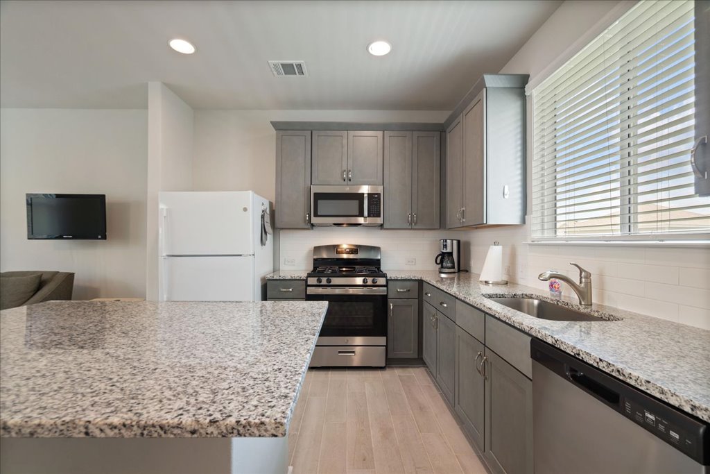 330 Hortus Drive Kyle, TX 78640 - Photo 11 of 26 a kitchen with granite countertop a sink a stove top oven a refrigerator and grey cabinets