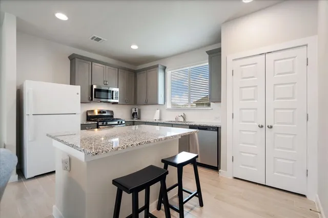 a kitchen with kitchen island granite countertop white cabinets refrigerator and microwave