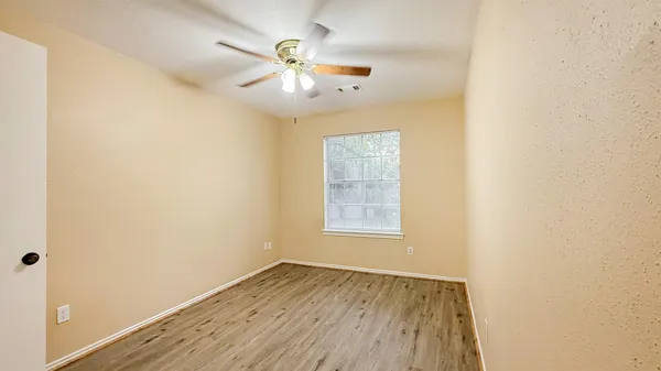 an empty room with wooden floor chandelier fan and windows