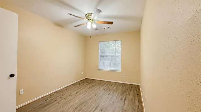 an empty room with wooden floor chandelier fan and windows