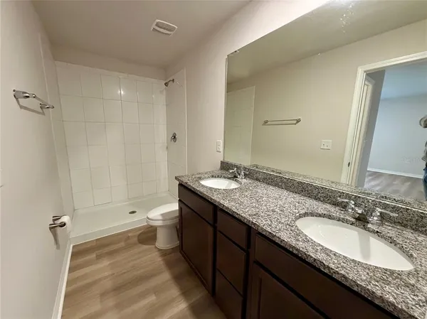 a bathroom with a granite countertop double vanity sink and mirror with shower