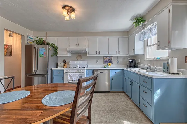 a kitchen with stainless steel appliances granite countertop a sink dishwasher a refrigerator a stove a dining table and chairs with wooden floor
