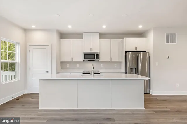 a kitchen with stainless steel appliances granite countertop a sink a stove a refrigerator and white cabinets with wooden floor