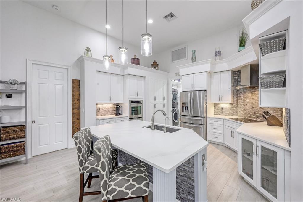7235 Mill Run Road Naples, FL 34109 - Photo 13 of 31 a kitchen with stainless steel appliances a stove a sink a kitchen island and chairs with wooden floor