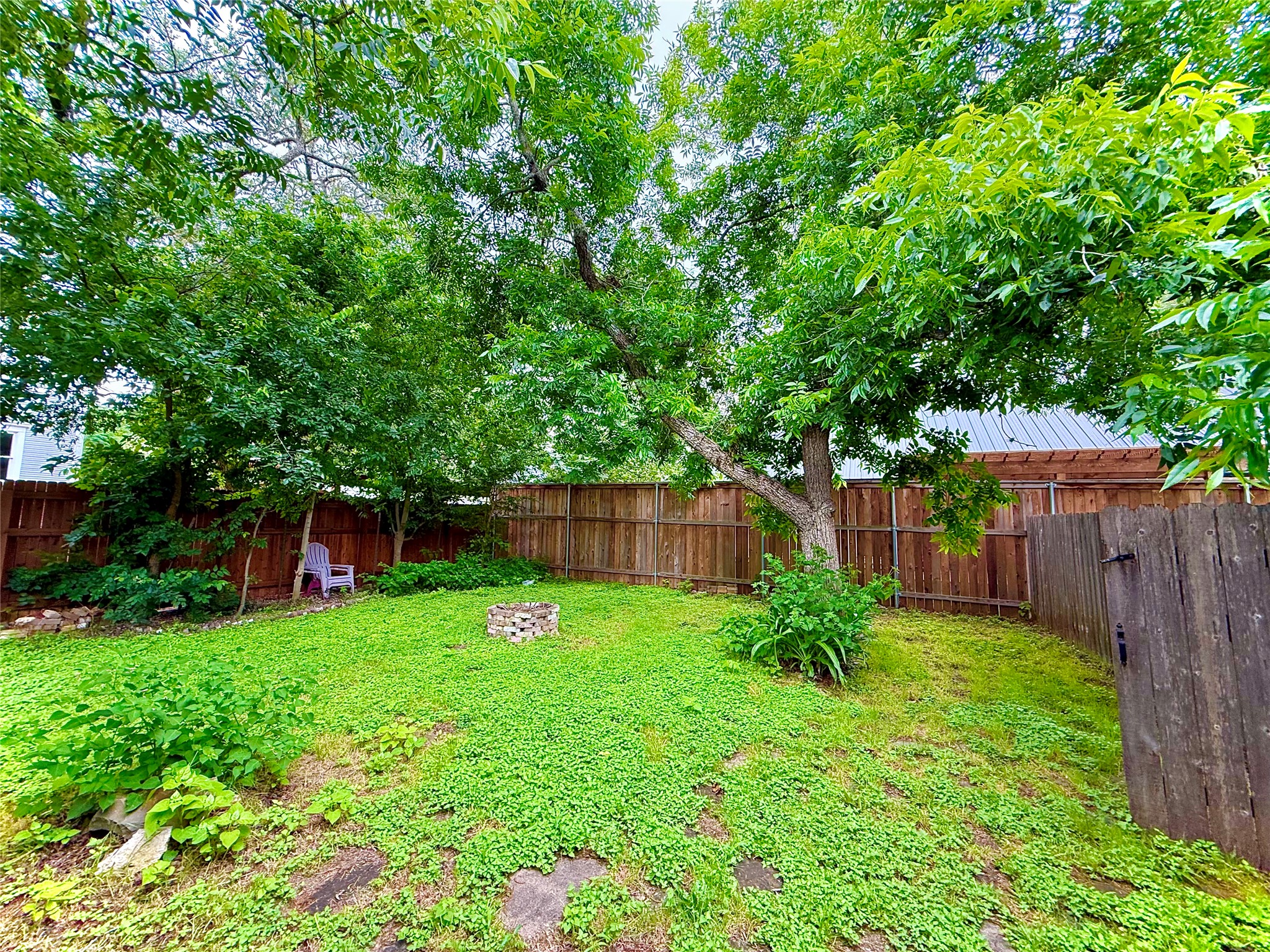 423 South Main Street Lockhart, TX 78644 - Photo 26 of 26 Expansive backyard featuring mature trees providing ample shade, a wood privacy fence, and a stone-lined fire pit